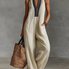 Beige sleeveless jumpsuit with high collar, zip front, and embroidered trim
