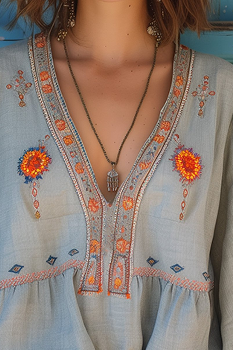 Light blue V-neck blouse with orange floral embroidery and decorative neckline trim