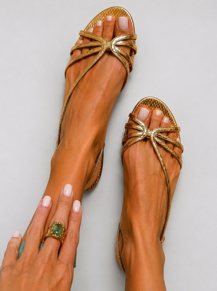 Gold strappy sandals with crisscross straps and bow detail at the toe.