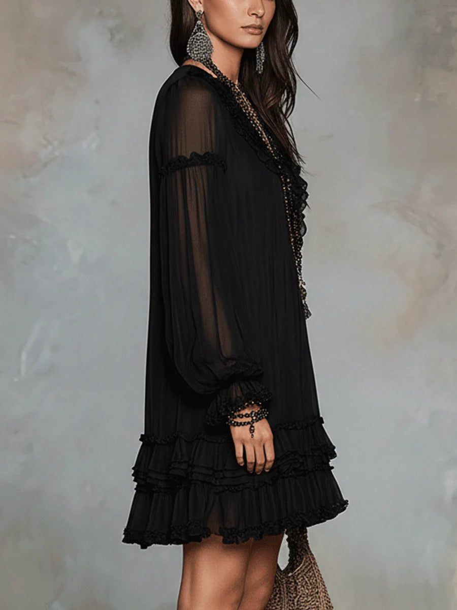 Black mini dress with sheer long sleeves and layered ruffle trim at hem and cuffs.