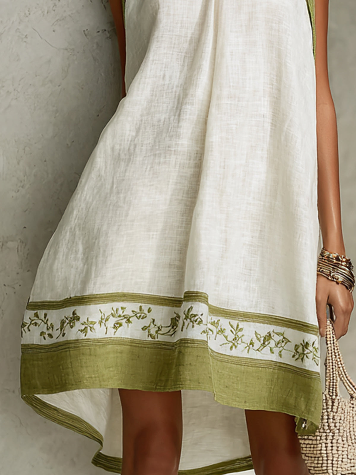 White midi dress with green floral hem band and draped sleeveless silhouette